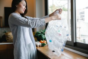 cheerful asian woman with heap of plastic bottles in kitchen