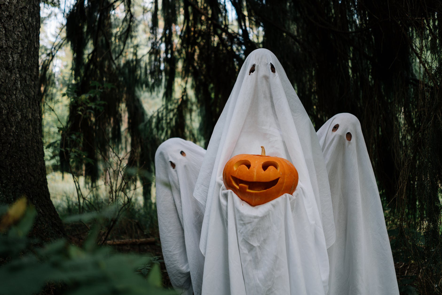 ghosts holding a carved pumpkin