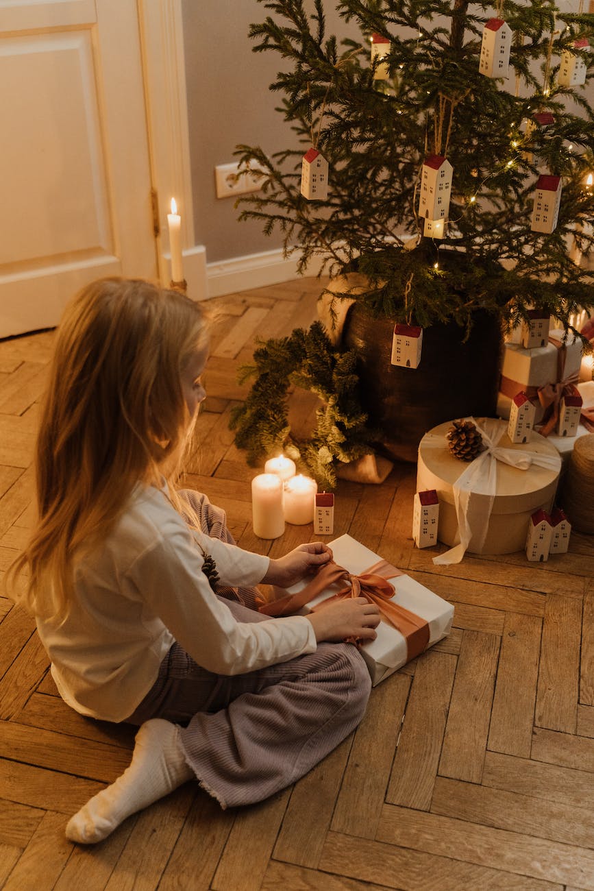 girl in white long sleeve shirt sitting on floor opening a gift